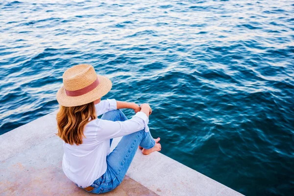 Sahilde oturan ve deniz manzarasının tadını çıkaran bir kadının yüksek açılı görüntüsü..