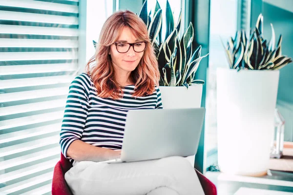 Lächelnde Reife Frau Sitzt Auf Stuhl Und Benutzt Laptop Während — Stockfoto