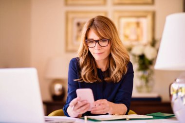 Çekici bir iş kadını dizüstü bilgisayarının arkasında otururken ve evde çalışırken mesaj atıyor. Merkez Ofis.