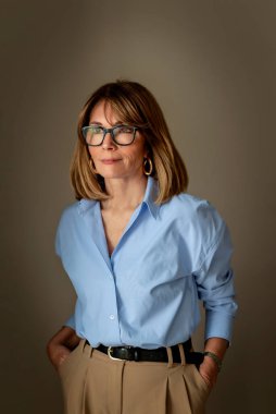 Kendine güvenen, orta yaşlı, omuz hizasında, sarı saçlı ve şık gözlükleri olan bir kadın. Mavi gömlek giyen ve düşünceli görünen çekici bir kadın. Yakın plan..