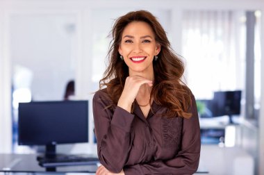 Ofiste kendine güvenen ve kameraya bakan bir iş kadını. Orta yaşlı profesyonel kadın iş kıyafeti giyiyor ve gülümsüyor. Boşluğu kopyala. 