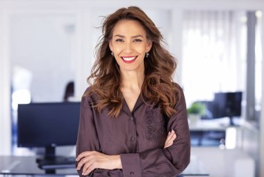 Ofiste kendine güvenen ve kameraya bakan bir iş kadını. Orta yaşlı profesyonel kadın iş kıyafeti giyiyor ve gülümsüyor. Boşluğu kopyala. 