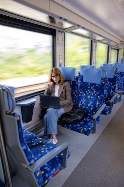 Trenle seyahat ederken dizüstü bilgisayarında çalışan sarışın kadın. Modern bir trende tek başına oturan kendinden emin bir kadın. Uzak çalışma.