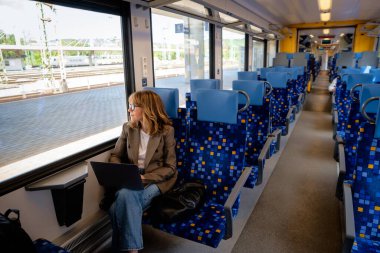 Trenle seyahat ederken dizüstü bilgisayarında çalışan sarışın kadın. Modern bir trende tek başına oturan kendinden emin bir kadın. Uzak çalışma.