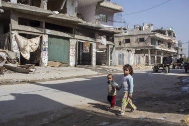 Shujayea, Gaza Strip/Palestine - feb 25 2015: brother and sister walk, among the semi-destroyed houses, holding hands.  clipart