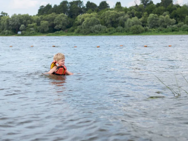 Cute little boy in orange life vest swimming in the river — Stock Photo, Image