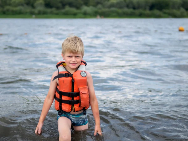 Cute little boy in orange life vest swimming in the river — Stock Photo, Image