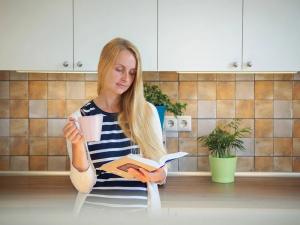 Blonde woman with cup of coffee is holding book — Stock Photo, Image