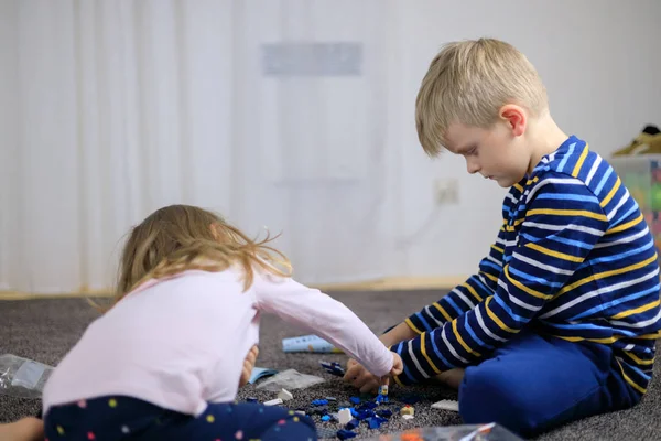 Zwei Kinder spielen mit vielen bunten Plastikklötzen. — Stockfoto