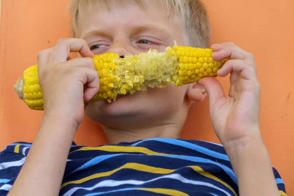 Kleiner Junge isst gekochten Maiskolben. — Stockfoto