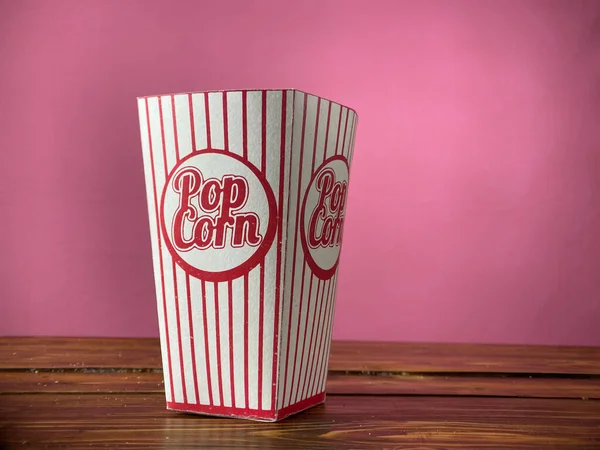 Попкорн в картонной коробке на розовом фоне — стоковое фото