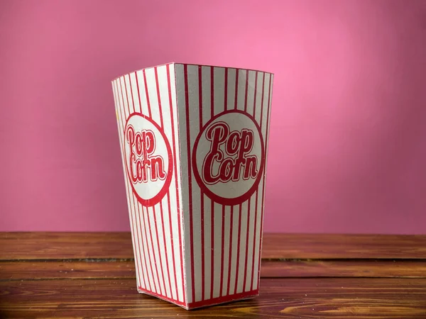 Попкорн в картонной коробке на розовом фоне — стоковое фото