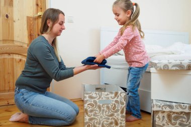 Mother and little daughter putting clothes to card box together clipart
