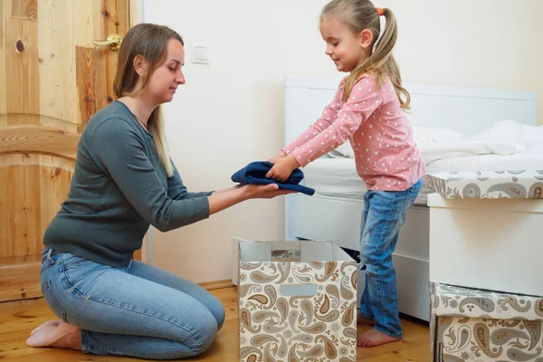 Мати і маленька донька разом кладуть одяг у картонну коробку Стокова Картинка