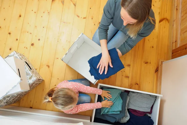 Mutter und kleine Tochter legen Kleidung in Karton zusammen — Stockfoto