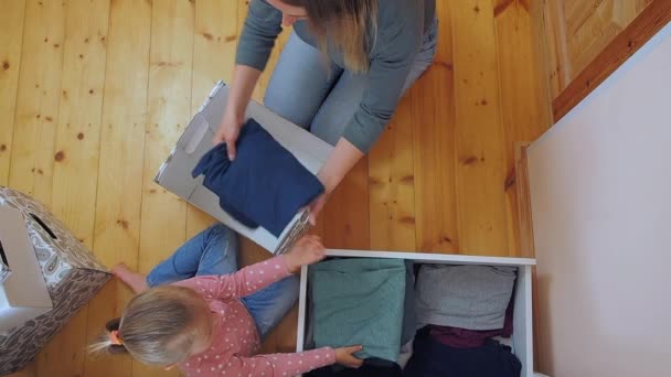 Mutter und kleine Tochter legen Kleidung in Karton zusammen — Stockvideo