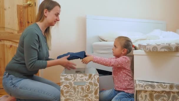 Mutter und kleine Tochter legen Kleidung in Karton zusammen — Stockvideo