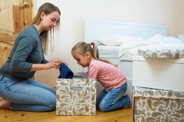 Anne ve küçük kız birlikte kağıt kutusuna kıyafet koyuyorlar.