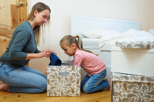 Mutter und kleine Tochter legen Kleidung in Karton zusammen — Stockfoto