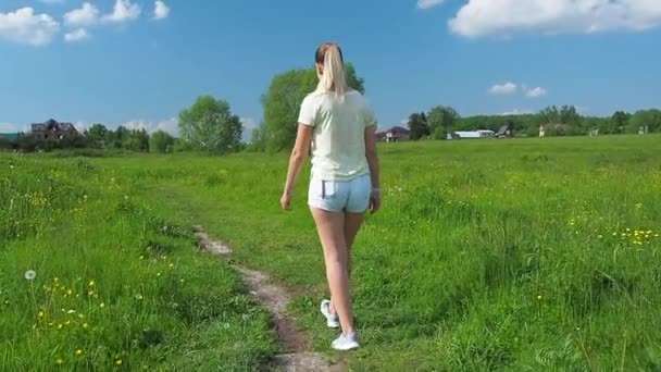 Молодая блондинка в джинсовых шортах ходит по лугу — стоковое видео