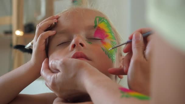 Mother drawing butterflies on face her baby daughter — Stock Video