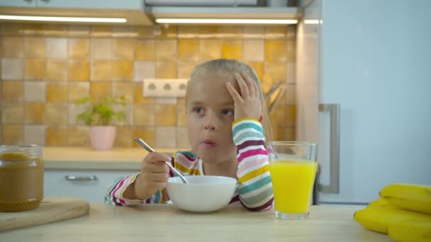 Маленькая голодная девочка ест хлопья с молоком и пьет сок — стоковое видео