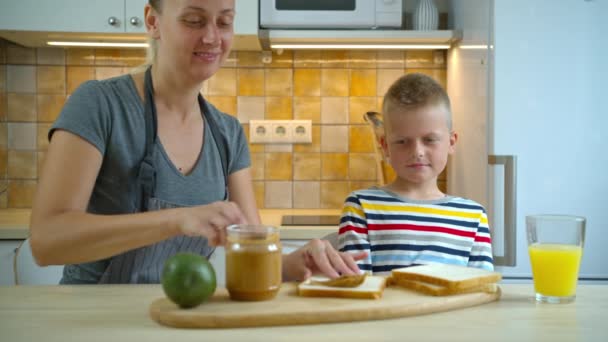 Matka przygotowuje kanapkę z masłem orzechowym jego syn — Wideo stockowe