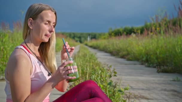 Sportig blond kvinna i parken dricker smoothie — Stockvideo