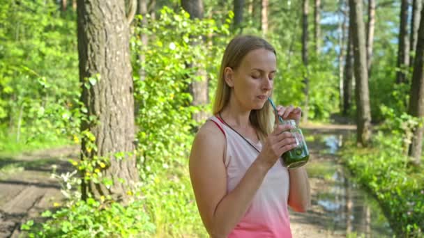 Sportliche blonde Frau im Park trinkt Smoothie — Stockvideo