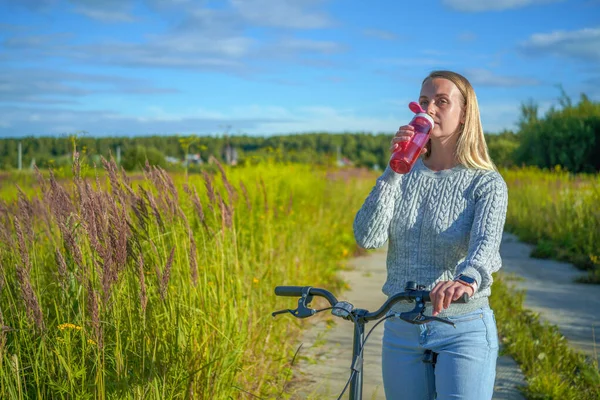 Young woman staying with bicycle and drinking water — Stock Photo, Image