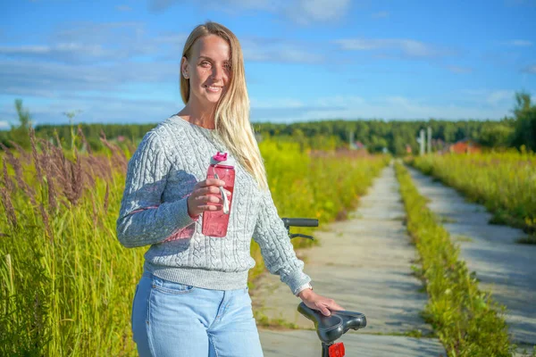 Young woman staying with bicycle and drinking water — Stock Photo, Image