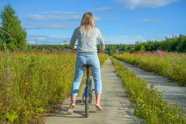 Donna in bicicletta nel paesaggio rurale, vista posteriore Foto Stock