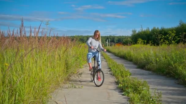 Feliz mujer sonriente montando en bicicleta en el paisaje rural — Vídeo de stock