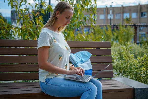 Dívka ve městě krajina sedí na lavičce s notebookem — Stock fotografie