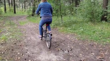 Kırsal yolda bisiklet süren kot pantolonlu bir kadın.