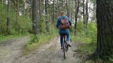 Kırsal yolda bisiklet süren kot pantolonlu bir kadın.