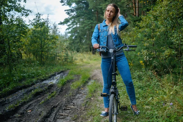 Nő farmerban biciklizik a vidéki úton — Stock Fotó