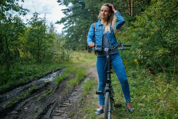 Woman in jeans riding on a bicycle at rural road — Stock Photo, Image