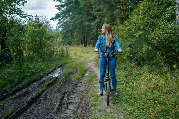 Woman in jeans riding on a bicycle at rural road — Stock Photo, Image