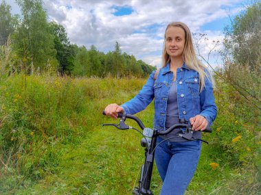 Kırsal yolda yürüyen bisikletli bir kadın.