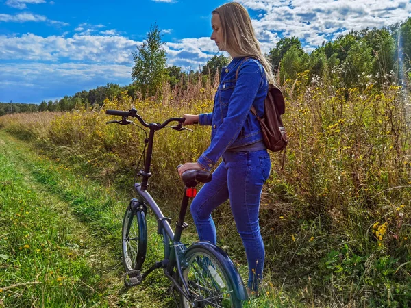 Žena v džínách na kole na venkovské silnici — Stock fotografie