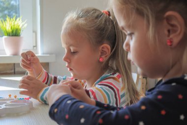 İki küçük kız boncuklardan bilezik yapıyor.