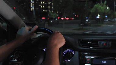 Geceleri şehir trafiğinde direksiyon başında direksiyon başında olan adamların yakın çekimi. Güvenli sürüş konsepti, araç kontrolü, ulaşım, araba içi ayrıntıları, aydınlanmış gösterge paneli ve modern şehir ortamında gece yolculuğu.