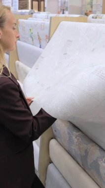 Koyu renk ceketli kadın, yenileme malzemesi seçerken hırdavatçıda duvar kağıdı rulosunu inceliyor. İç tasarım, duvar kaplaması, dekoratif ev dekorasyonu, DIY yaşam tarzı ve modern dekorasyon alışverişi kavramı..