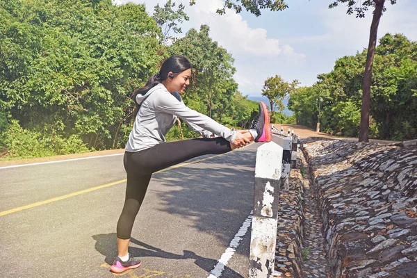 Woman is stretching before jogging in the forest mountain road