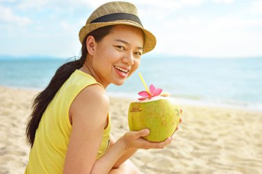 Taze hindistan cevizi suyu içme ve yaz plaj tatil üzerinde oturan mutlu kadın