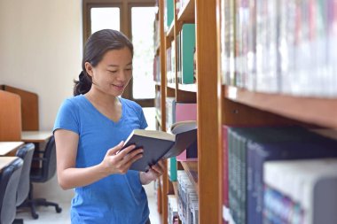 Kadın kütüphanede kitap okuyor.