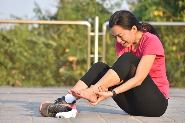 Female runner touching foot in pain due to sprained ankle — Stock Photo, Image