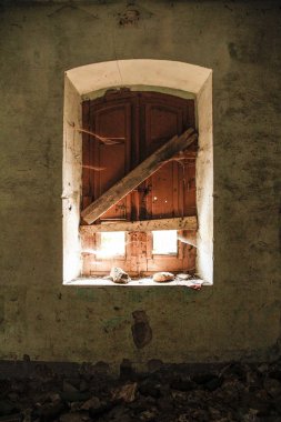 Window of an abandoned house taken from inside; the light illuminates the room a little, leaving a glimpse of the cobwebs and the peeling wall