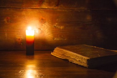 Antik çağda okuma sahne: eski bir kitap harap ahşap masanın üzerine eğilerek ışıklı bir mum tarafından ahşap bir arka plan üzerinde